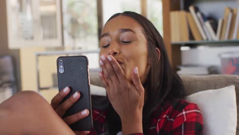 Mixed-race-woman-using-smartphone,-having-a-video-conversation-blowing-kisses