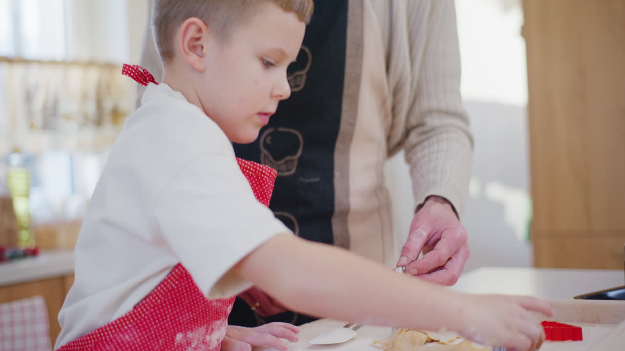 el niño ayuda a su padre a hacer galletas de pan de jengibre para navidad y corta castañas de la masa.