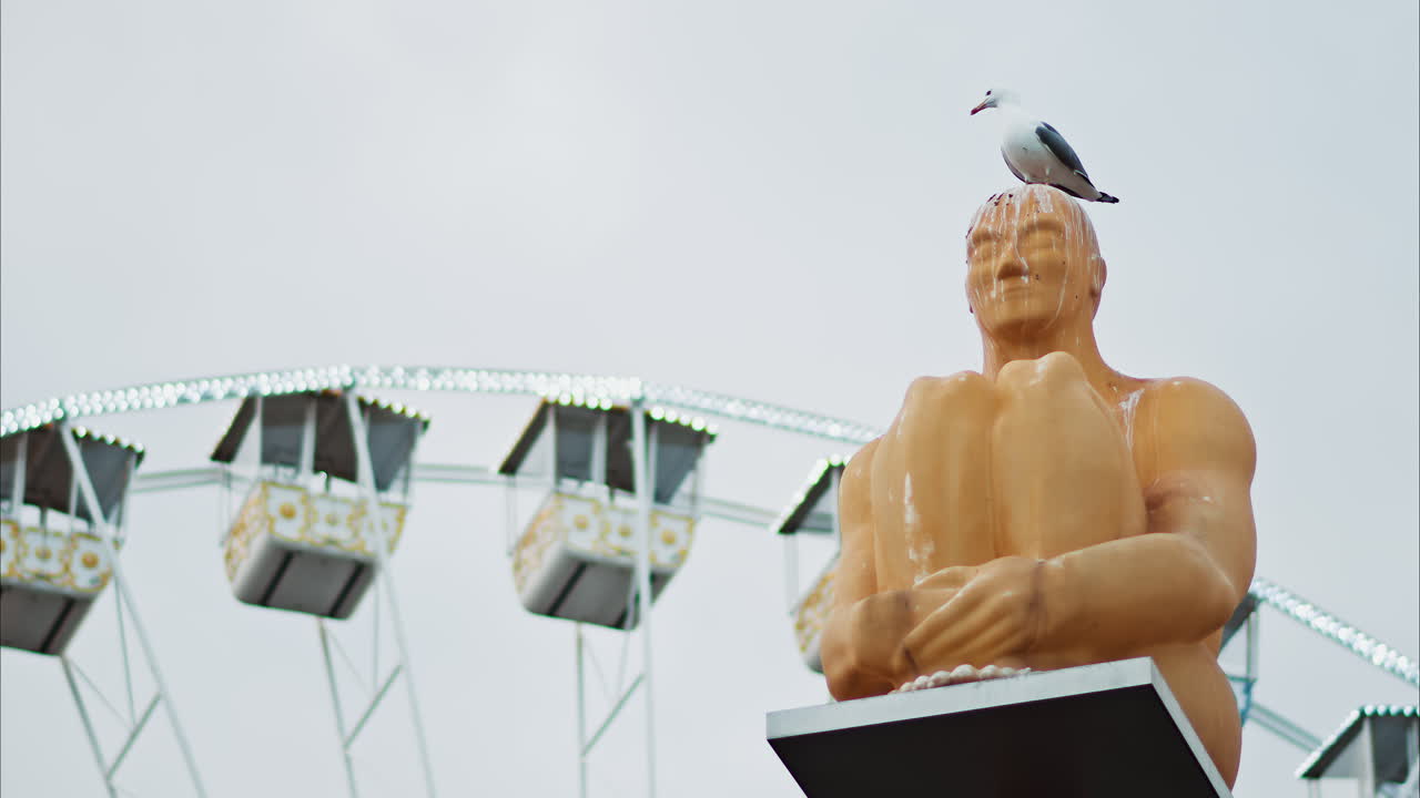 Nice, France - December 8, 2024: Seagull standing on the Conversation a Nice statue by Jaume Plensa at Place Massena with a ferris wheel on the background