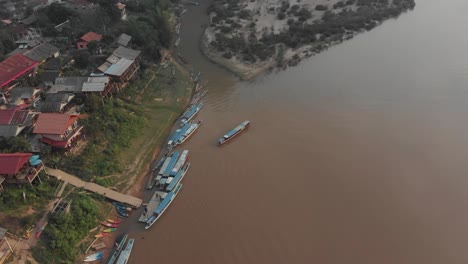 Vista-De-Arriba-Hacia-Abajo-De-Muang-Ngoy-Con-Barcos-En-El-Río-Nam-Ou-Durante-La-Puesta-De-Sol,-Aérea