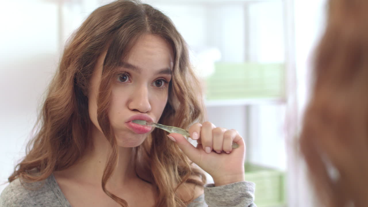Young woman brushing teeth in mirror at home bathroom. Girl cleaning teeth