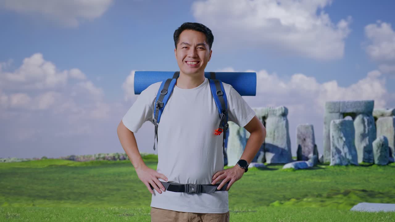 Asian Male Hiker With Mountaineering Backpack Smiling And Posing Arms Akimbo While Traveling In Stonehenge