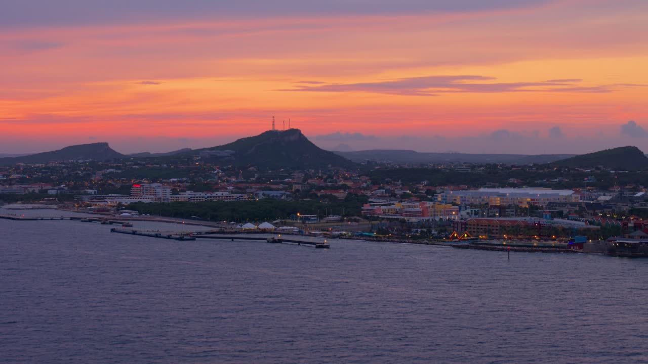 Aerial view of Seru Piscadera with Christoffelberg in the distant background during sunset, capturing the rugged landscape of Curacao, orange yellow haze from dusk in sky