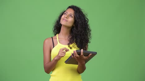 young beautiful hispanic woman thinking while using digital tablet