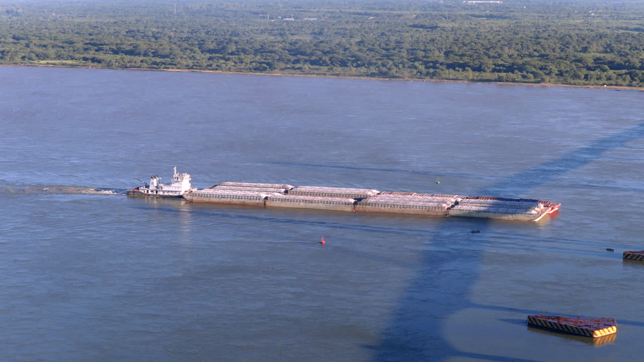 Cargo barge vessel traveling through the Paraná River waterway with agricultural landscape visible along the banks
