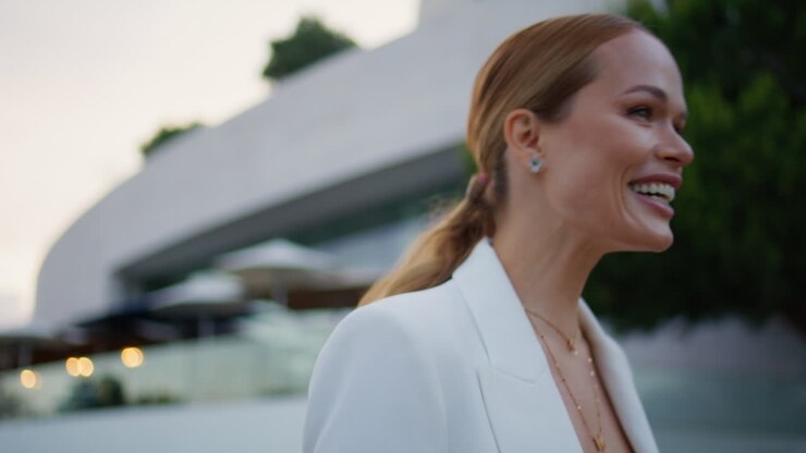 Ritratto di donna d'affari sorridente che cammina per una strada di sera in elegante tailleur bianco.