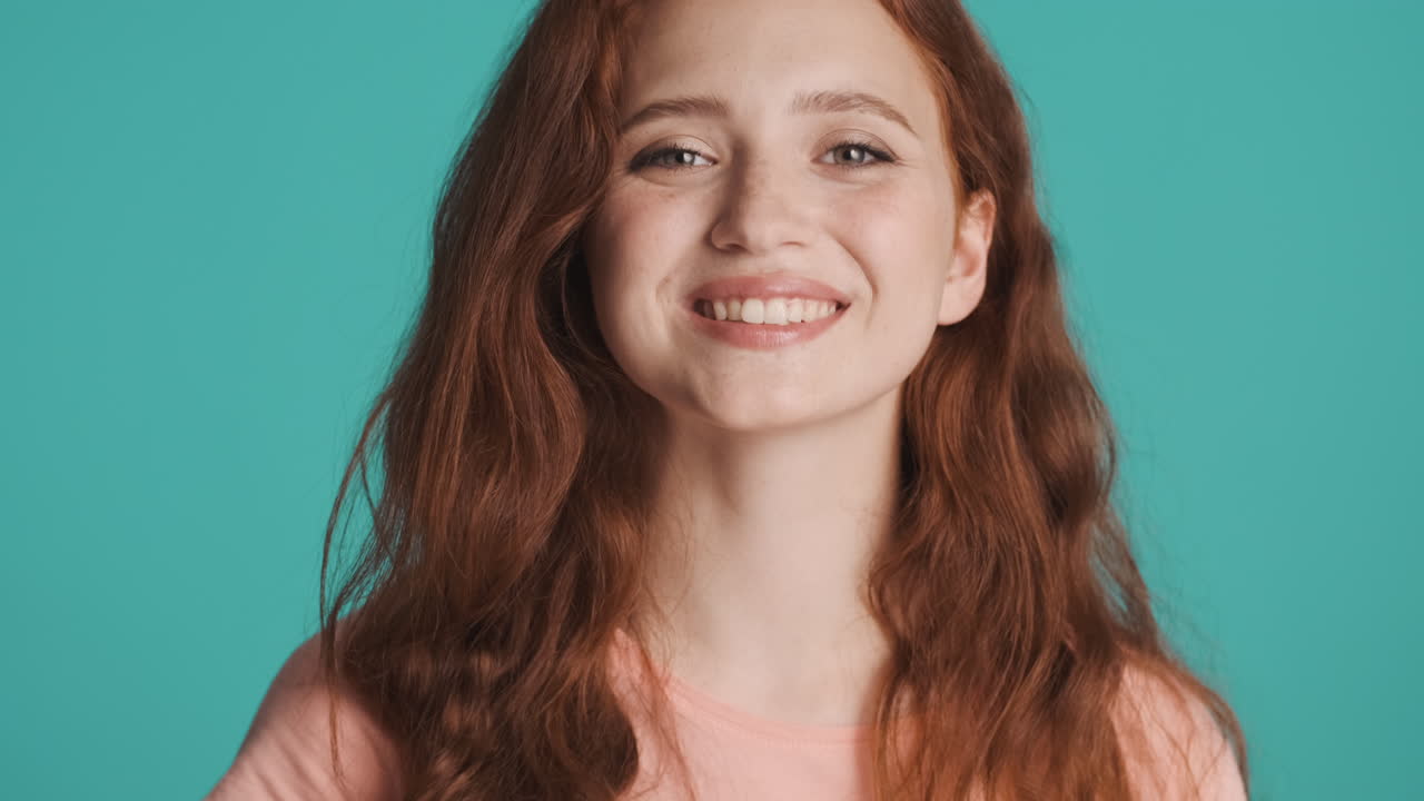 Redheaded girl in front of camera on turquoise background.