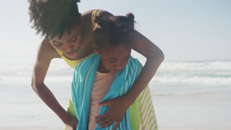 african american mother drying her daughter with a towel at the beach