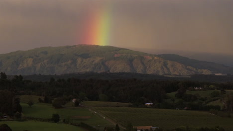 drone shot of rolling hills, rainbow, and mist-covered mountain range, tasman district, new zealand