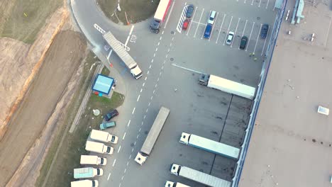 Aerial-view-of-a-semi-trucks-with-cargo-trailers-standing-on-warehouses-ramps-for-loading-unloading-goods-on-the-big-logistics-park-with-loading-hub