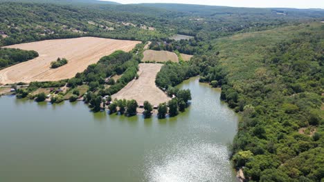 water surrounded by trees and hills in slovakia, with hay bale farm in distance