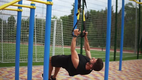 deportista caucásico haciendo ejercicios de flexión usando un cinturón de goma para forzar la fuerza del entrenamiento al aire libre