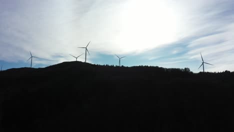 Silhouette-of-wind-turbines-against-bright-sky-with-dark-mountain-foreground---5-rotating-turbines-at-Midtfjellet-windpark-Fitjar-Norway