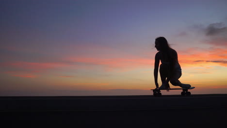 hermosa chica monta una patineta en la carretera contra el cielo al atardecer