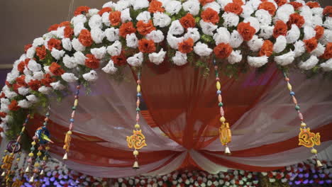 vibrant colorful indian hindu wedding decorations on the main stage with flowers, drapes and ornaments hanging from top. slow motion.