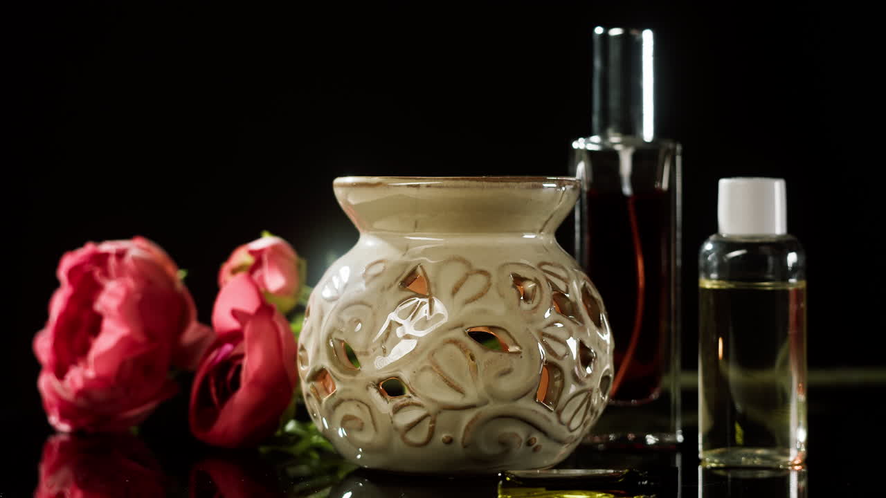 Main plaçant un flacon d’huile essentielle à côté d’une lampe à parfum et de fleurs