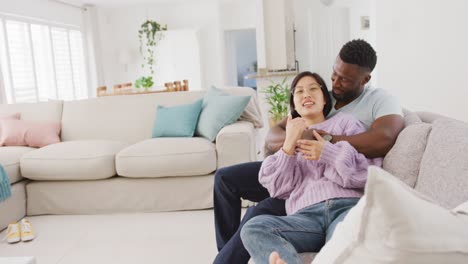 diverse couple sitting on couch and embracing in living room