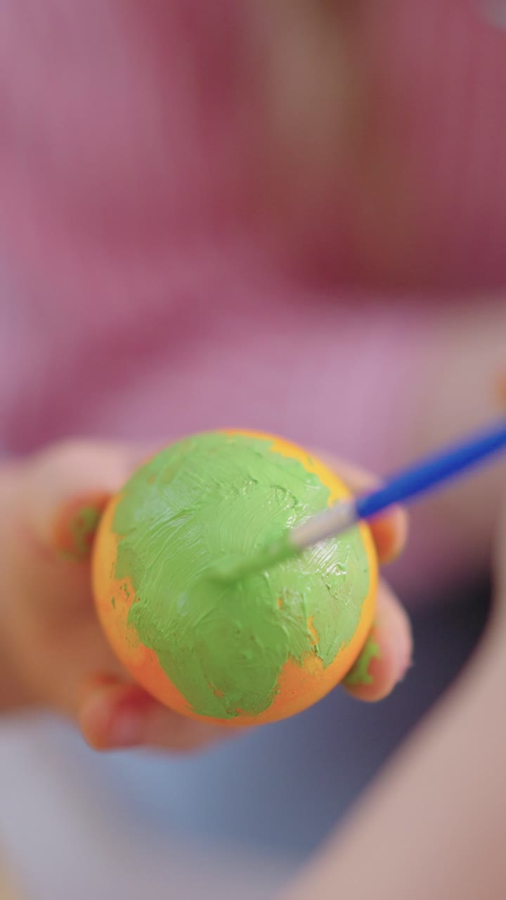 Close-up de Mão Pintando um Ovo Laranja com Tinta Verde