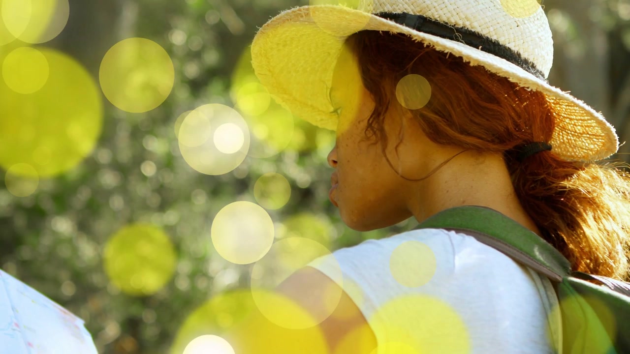 Mulher com chapéu de palha e mochila verde virando, movendo o braço para viajar, com bokeh amarelo atraindo o olhar.
