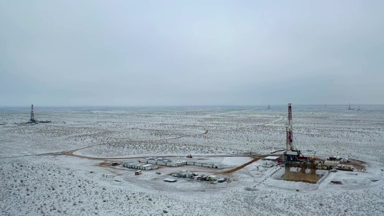 Olieboreplatform i drift i et sneklædt ørkengasfelt under en overskyet himmel.