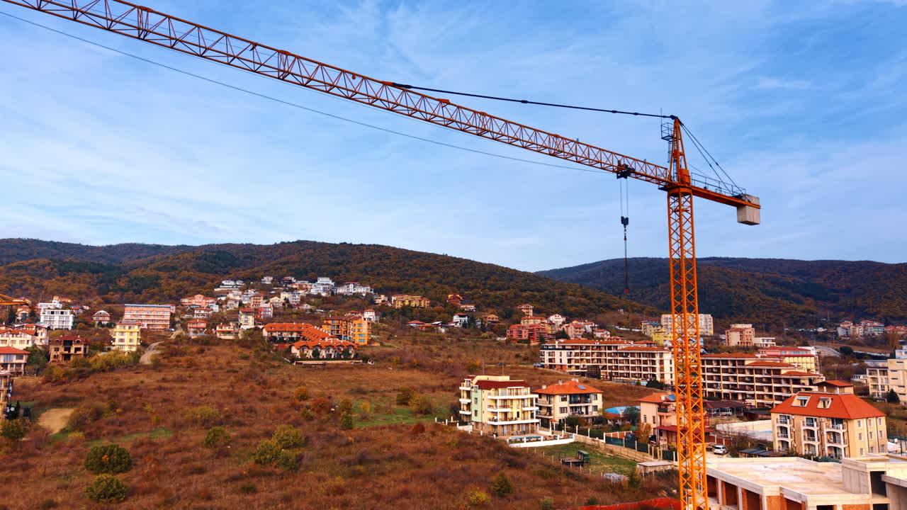 Una gru edile si erge alta sopra i nuovi edifici in una posizione collinare. Una gru edile è al lavoro in un cantiere edile vicino a una collina con delle case
