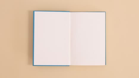 blue hardcover vintage book appear and open with copy space on beige background. stop motion flat lay