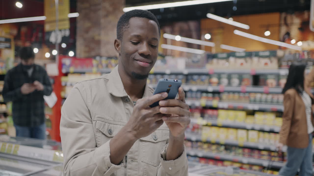 Mann kauft im Supermarkt ein und nutzt dabei sein Smartphone