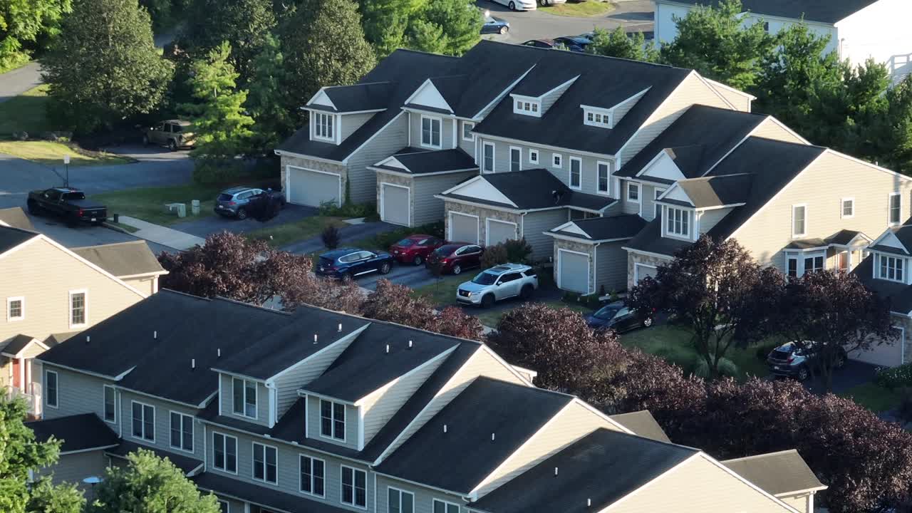 Aerial drone view of modern American suburban townhouses with attached garages, multiple parked cars and green trees. Peaceful residential architecture and lifestyle in USA. Summer season