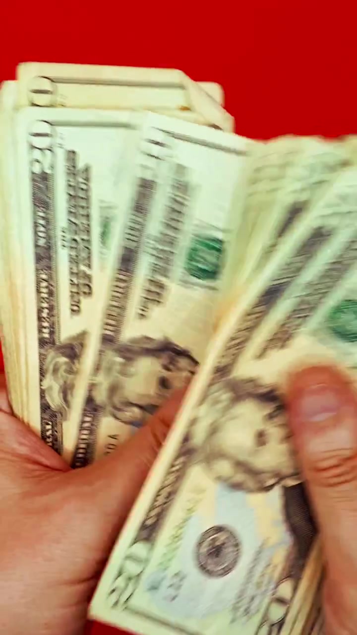 B-roll verticale 9:16: mani che sventolano banconote da 20 dollari su sfondo rosso. Concetto per denaro veloce, motivazione alla ricchezza, transazione illegale, pagamento dello stipendio, affari del dark web e successo finanziario.