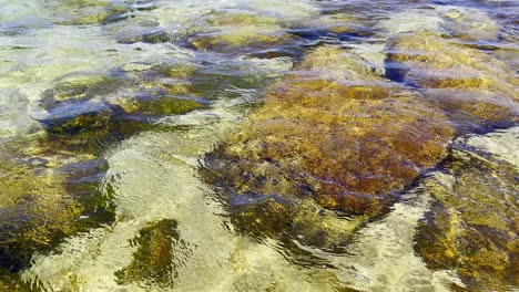 Océano-Claro-Que-Muestra-El-Fondo-Marino-Lleno-De-Rocas-Y-Algas-Pequeñas-Olas-En-La-Superficie