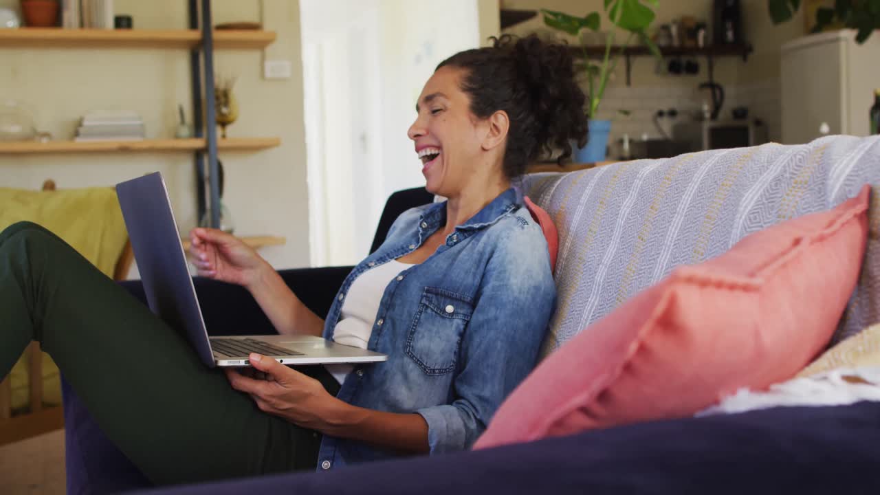 Smiling caucasian woman using laptop on video call, sitting on sofa at home
