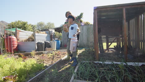 Senior-biracial-grandmother-and-grandson-holding-basket-with-vegetables-in-sunny-garden,-slow-motion