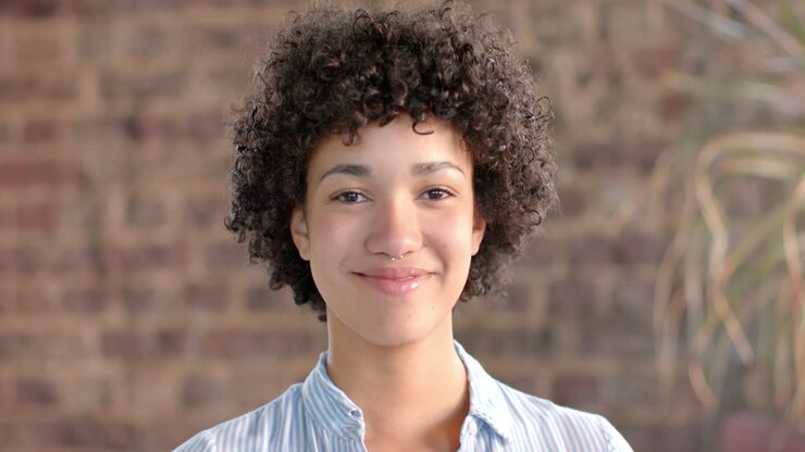 Portrait of happy biracial casual businesswoman with curly hair in office in slow motion