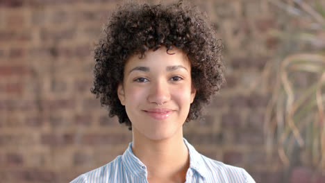 Portrait-of-happy-biracial-casual-businesswoman-with-curly-hair-in-office-in-slow-motion