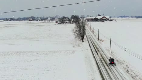 aerial tracking shot of amish horse and buggy on rural country road during winter snowstorm