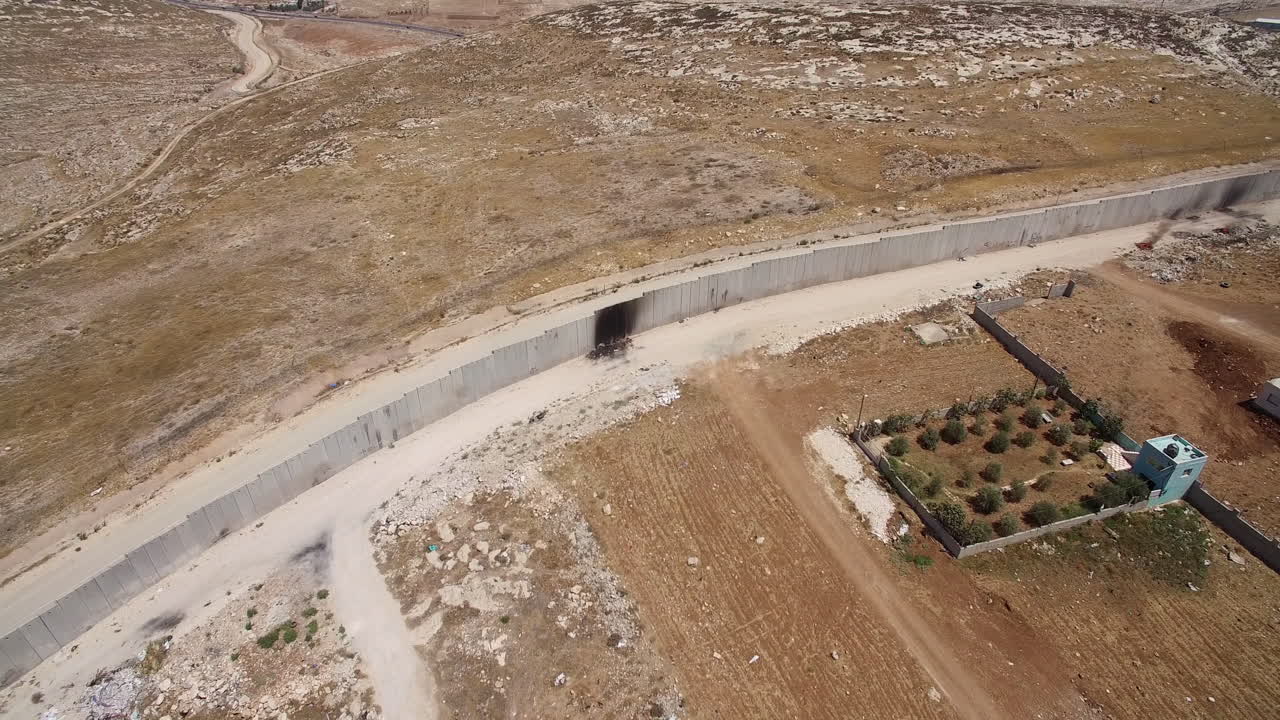 Aerial view of a concrete security wall in a dry, arid landscape