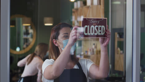 female hairdresser wearing face mask changing sign board from closed to open at hair salon