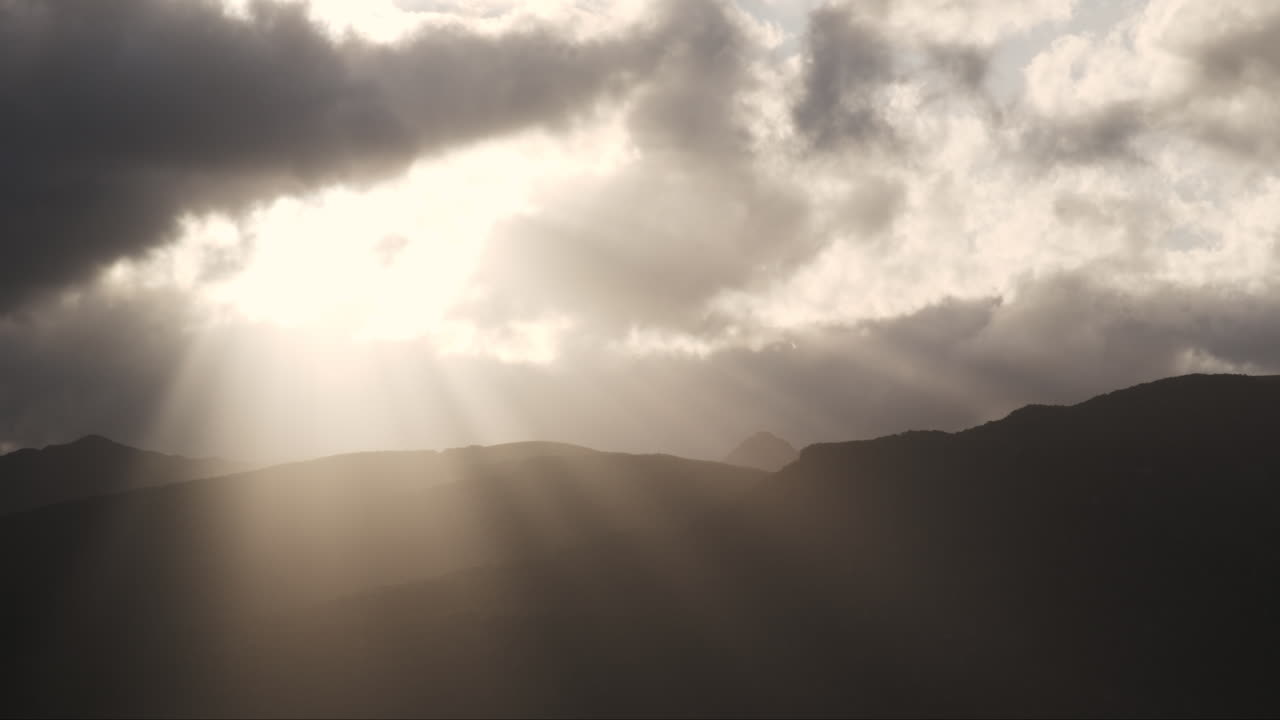 Mythic sun ray beams shining through clouds over mountain silhouette