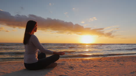 Young-Woman-With-Long-Hair-Sitting-On-The-Beach-At-Sunset-Meditating-Calm-Self-Confidence-And-Health