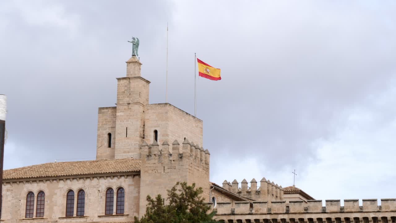 Bottom up shot showing spanish flag waving in wind on top of Cathedral de Mallorca against cloudy sky