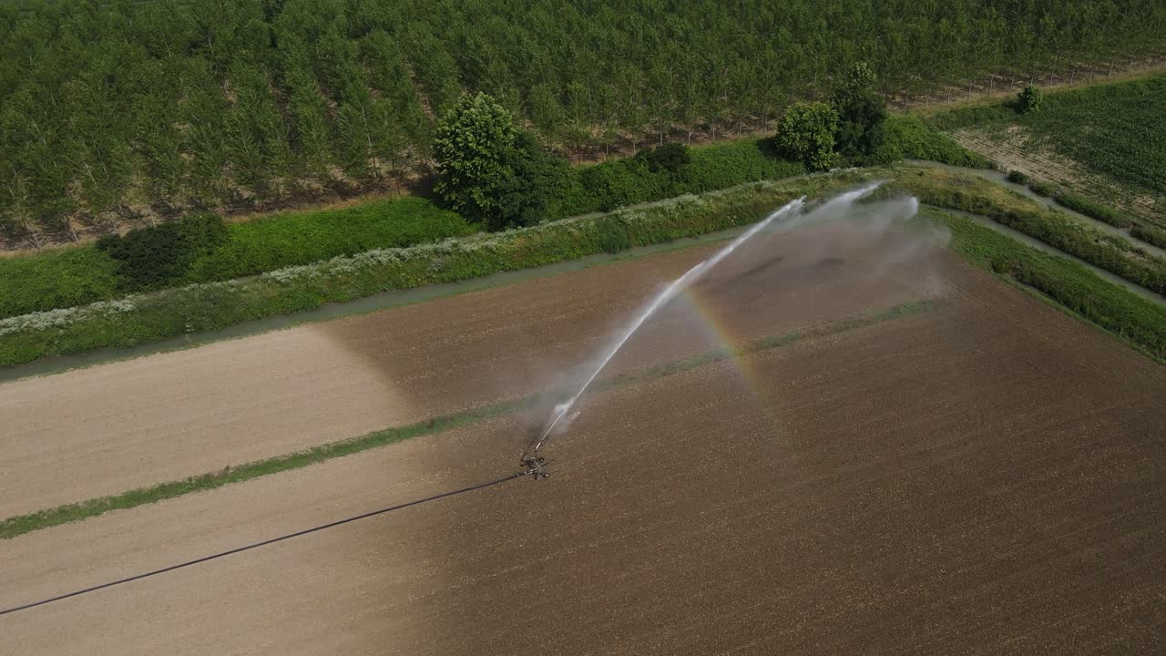Aerial drone footage of a water sprinkler irrigating newly sown farmland in Italy, rotating anti-clockwise into a near top-down view