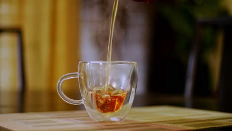 tight shot of an african american man pouring steaming hot tea into a transparent glass tea cup