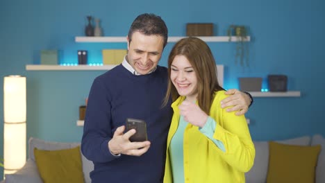padre alegre y hija joven adulta mirando el teléfono. se alegran.