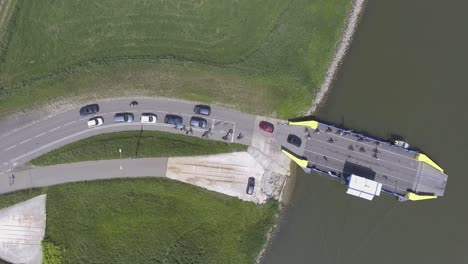 una toma de arriba hacia abajo de un ferry con un dron, cargando autos y personas desde un río hasta tierra, toma con trípode, en los países bajos