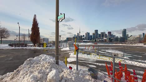 a scenic view of the toronto skyline as seen from polson street, surrounded by snow banks and marked by orange construction cones, capturing the city's urban winter charm