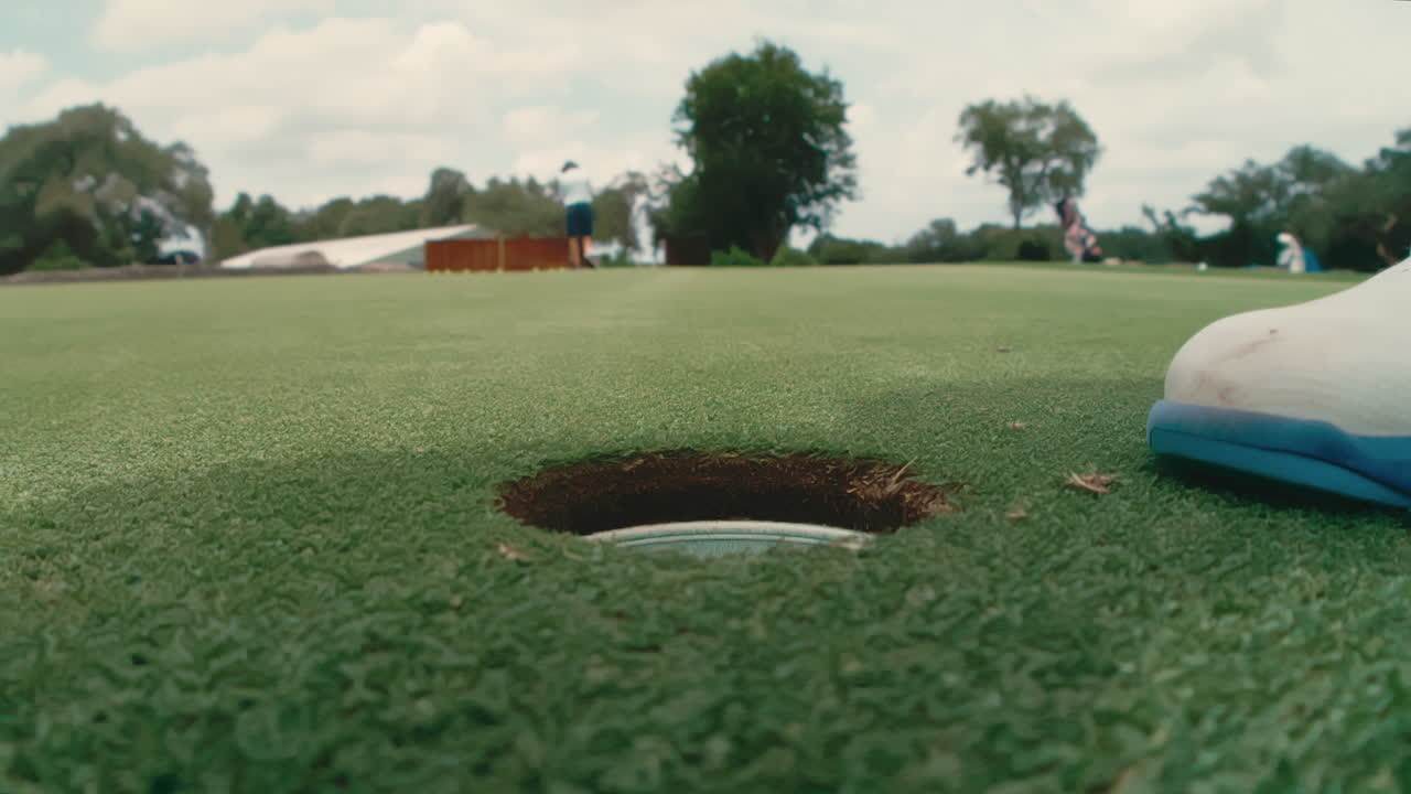 Extreme slow motion of golfer’s foot approaching the hole and reaching in to pick up golf ball after sinking putt on green, highlighting precision and victory moment