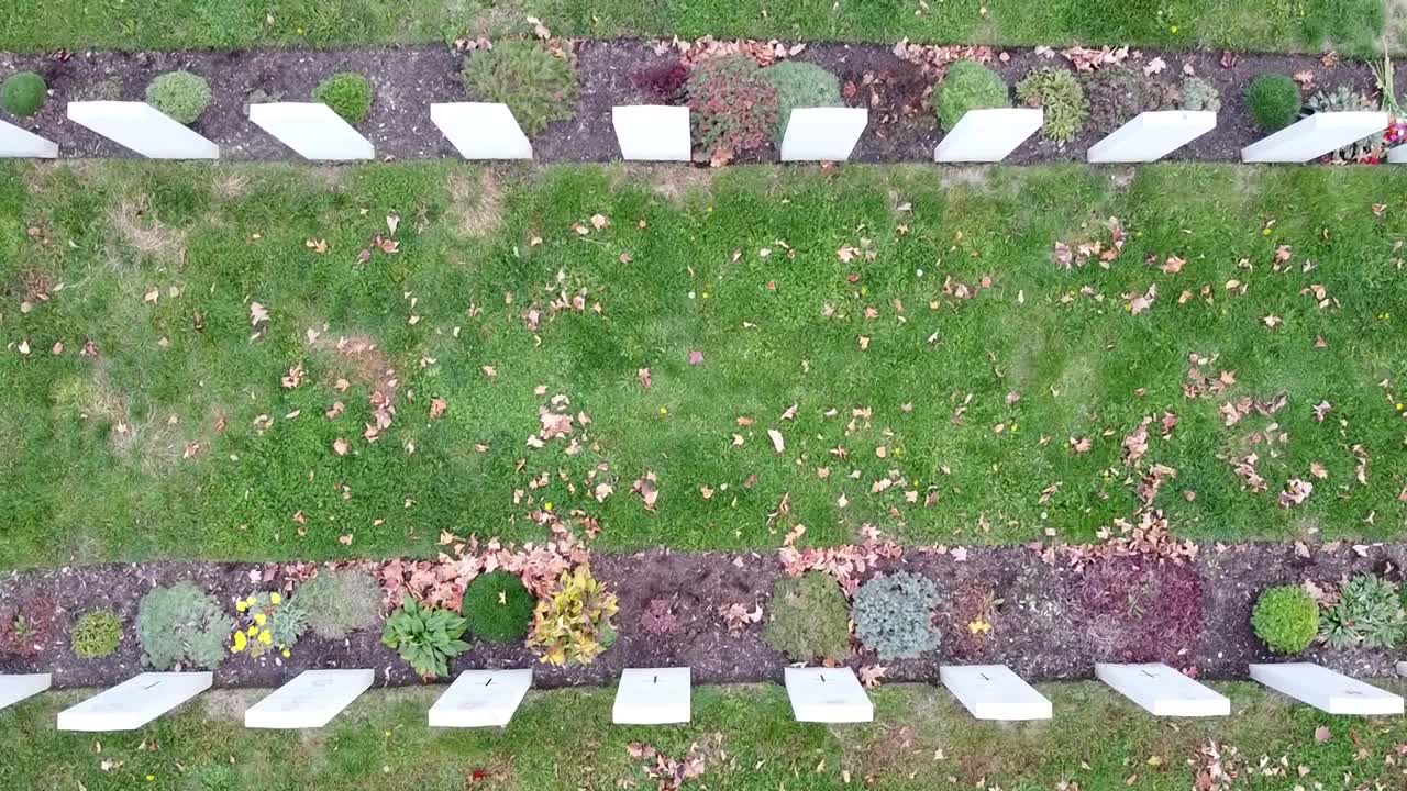 Drone flies over rows of cemetery headstones with a birdseye view.