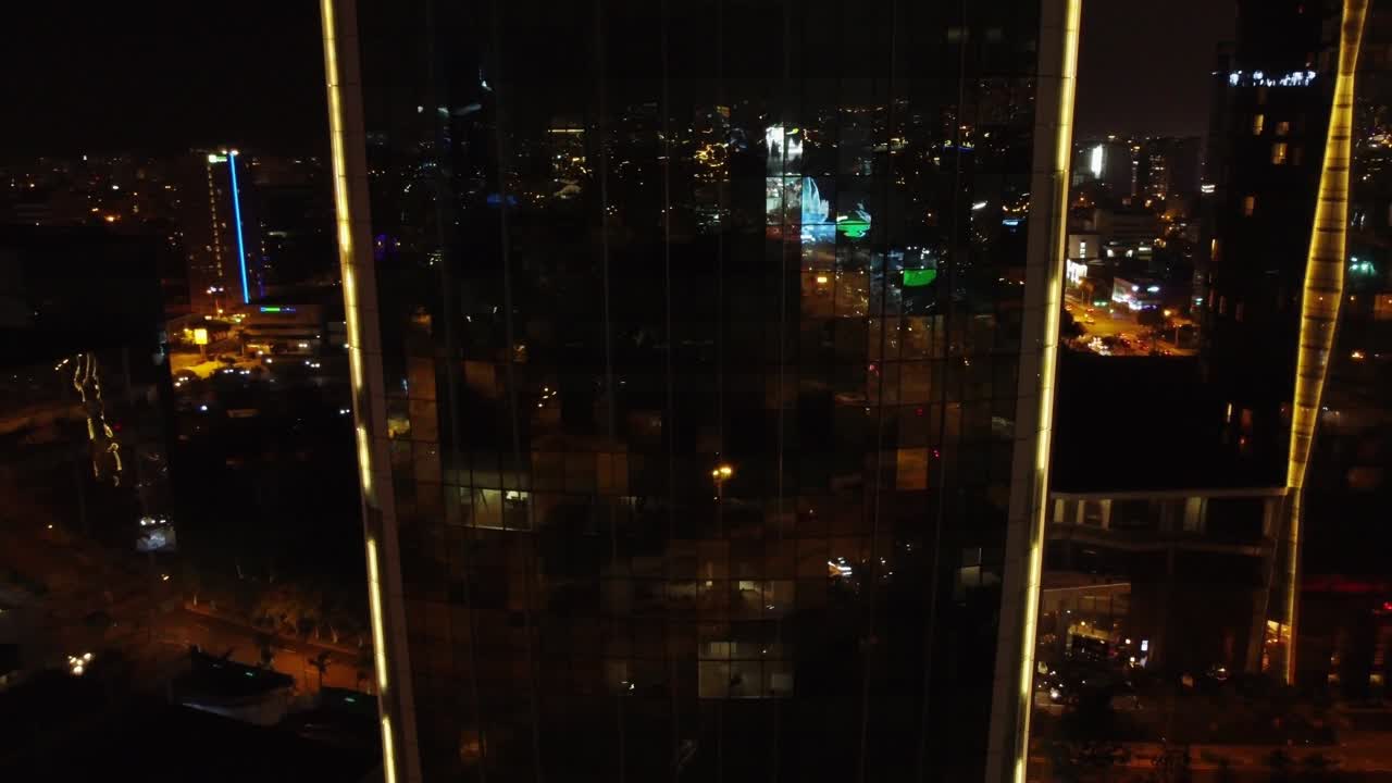 Night time drone video orbiting around a tall building. City lights reflect off of the skyscraper's windows. Located in Lima, Peru