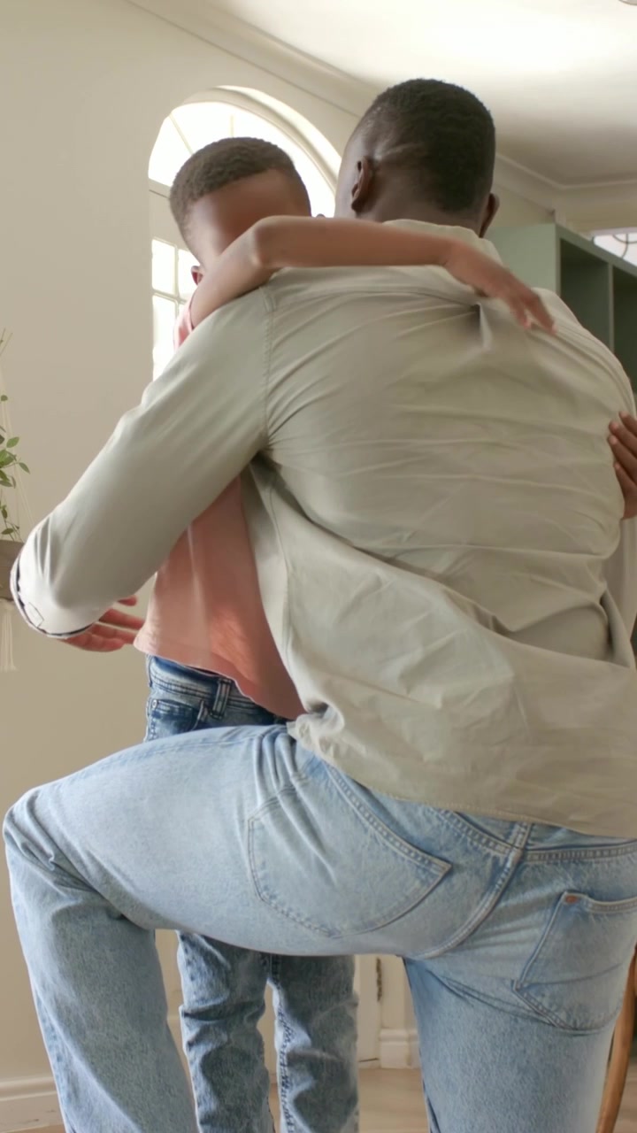Video verticale: Padre inginocchiato con le braccia aperte, il figlio lo abbraccia alla porta d'ingresso, ricongiungendosi.