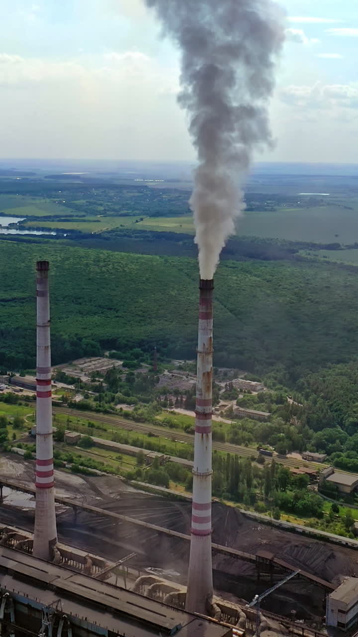 Industrial area in nature. Industrial pipes with smoke. Metallurgical factory with pipes among green field. Aerial view. Vertical video